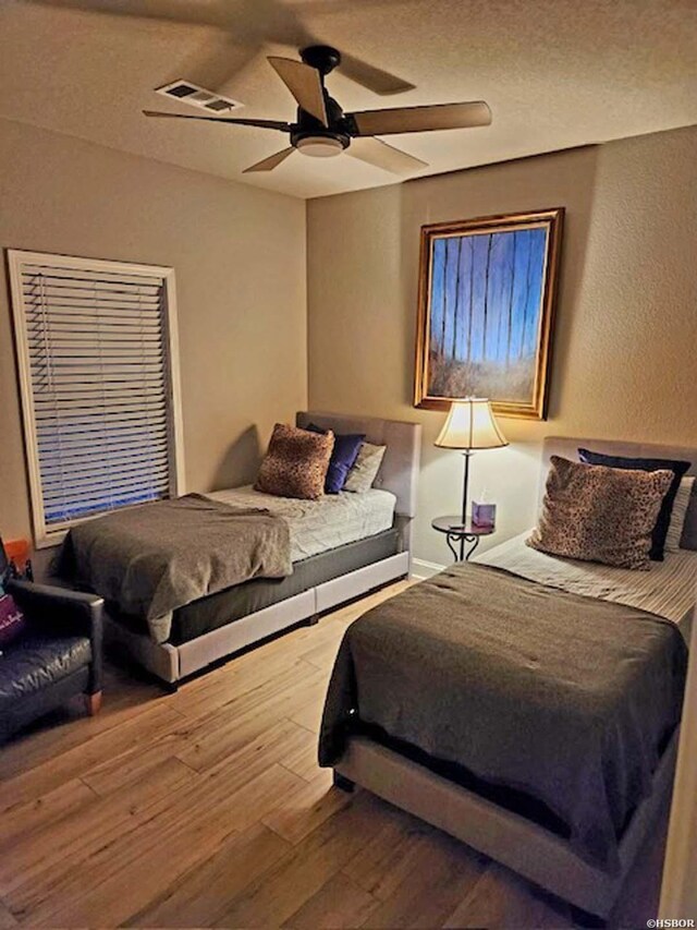 bedroom with ceiling fan, a textured ceiling, wood finished floors, and visible vents