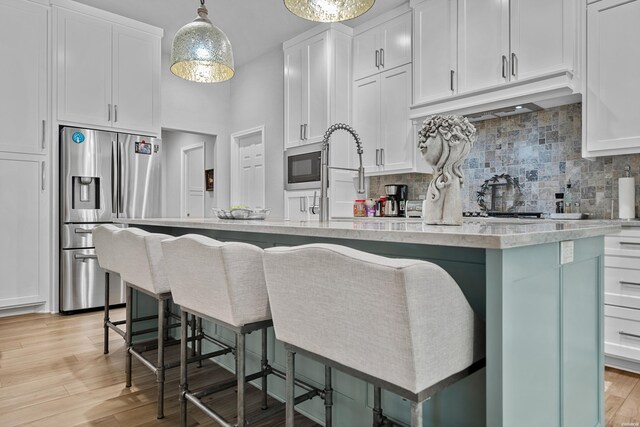 kitchen with white cabinets, light countertops, a kitchen island with sink, and stainless steel fridge with ice dispenser