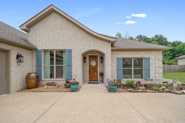 view of front facade featuring a patio area, roof with shingles, fence, and brick siding