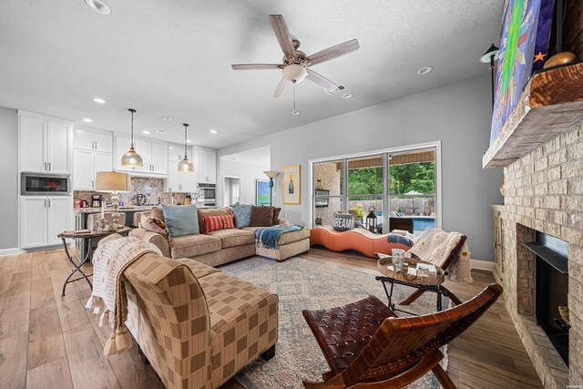 living area featuring ceiling fan, a textured ceiling, light wood-type flooring, a fireplace, and recessed lighting