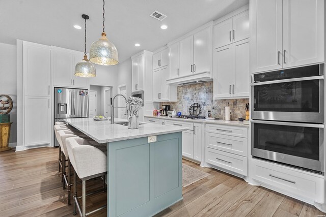 kitchen with pendant lighting, visible vents, appliances with stainless steel finishes, a kitchen island with sink, and white cabinets