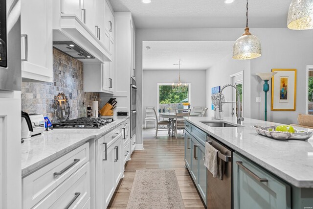 kitchen with a sink, white cabinets, hanging light fixtures, appliances with stainless steel finishes, and a center island with sink