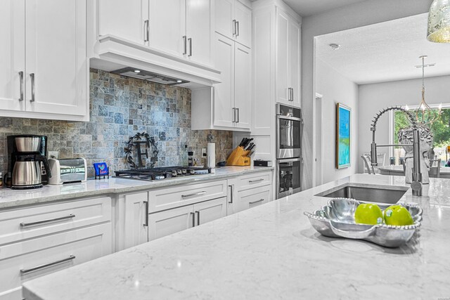 kitchen with white cabinetry, a sink, hanging light fixtures, and custom exhaust hood