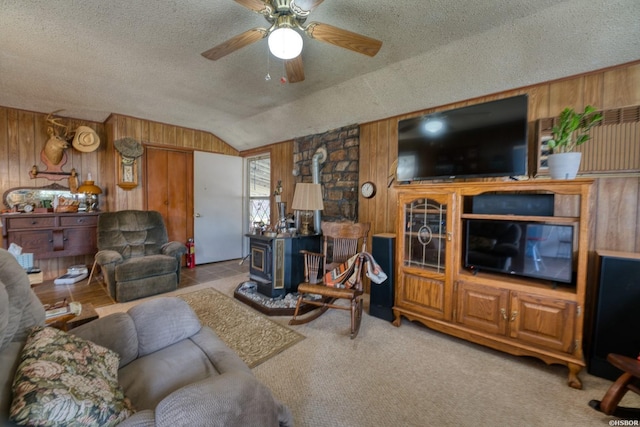 living room featuring wooden walls, lofted ceiling, ceiling fan, a wood stove, and a textured ceiling