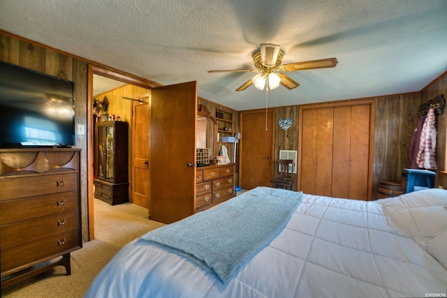 bedroom with light carpet, wood walls, ceiling fan, and a textured ceiling