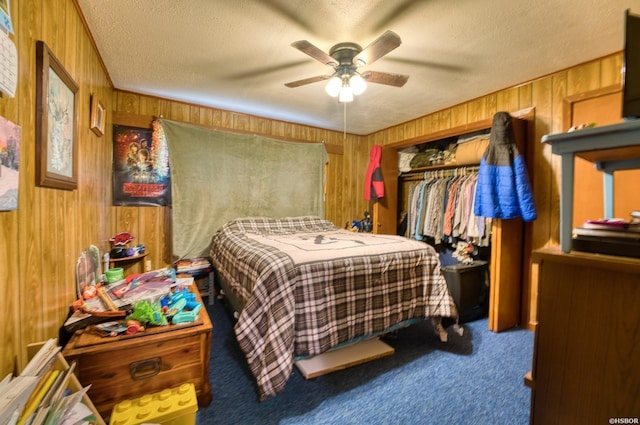 carpeted bedroom with a closet, wooden walls, a ceiling fan, and a textured ceiling