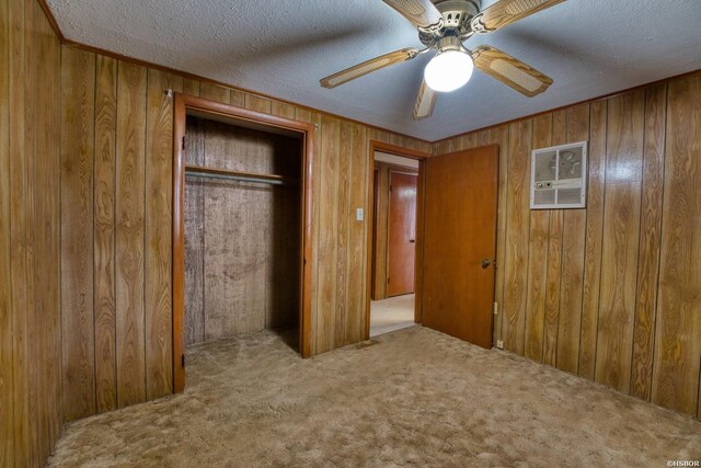 unfurnished bedroom featuring wooden walls, a ceiling fan, a textured ceiling, carpet floors, and a closet