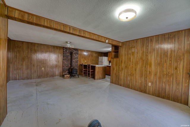 finished below grade area with freestanding refrigerator, a wood stove, wooden walls, and a textured ceiling