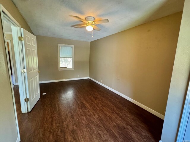 empty room with ceiling fan, baseboards, and dark wood-type flooring