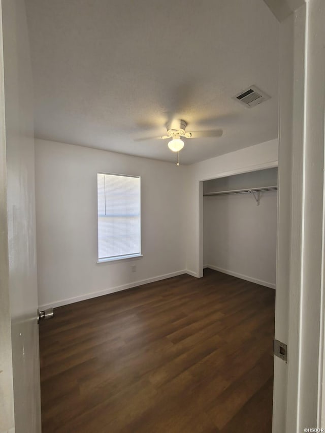 unfurnished bedroom featuring a ceiling fan, visible vents, baseboards, a closet, and dark wood finished floors