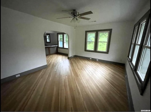 unfurnished living room featuring baseboards, visible vents, arched walkways, ceiling fan, and dark wood-type flooring