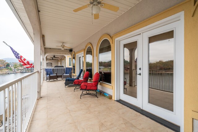 view of patio with ceiling fan, french doors, a water view, and a balcony