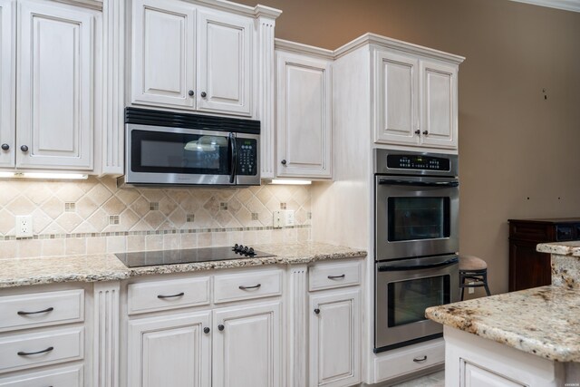 kitchen featuring stainless steel appliances, backsplash, light stone countertops, and white cabinets