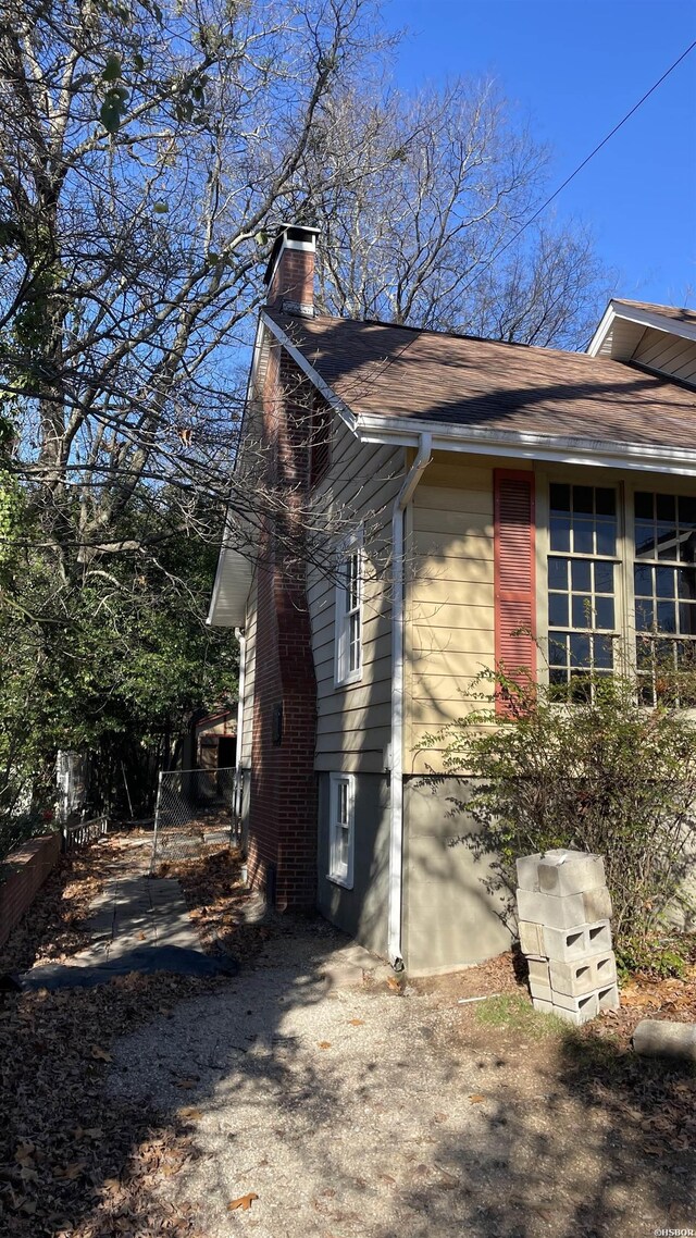 view of side of property with a shingled roof, a chimney, and fence