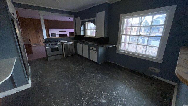 kitchen featuring a healthy amount of sunlight, dark countertops, appliances with stainless steel finishes, and ornamental molding