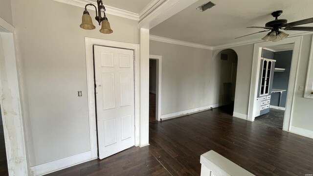 empty room with arched walkways, dark wood finished floors, crown molding, ceiling fan, and baseboards