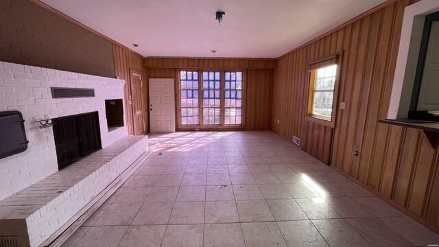 unfurnished living room with plenty of natural light, wooden walls, visible vents, and a fireplace