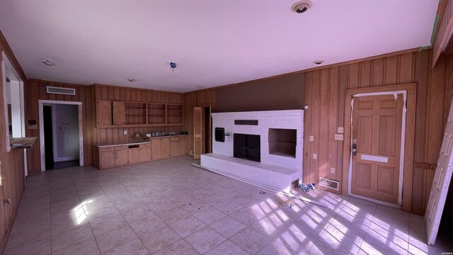 unfurnished living room with ornamental molding, wood walls, a brick fireplace, and visible vents