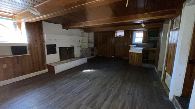 unfurnished living room with wooden walls, a fireplace with raised hearth, wooden ceiling, dark wood-type flooring, and beamed ceiling