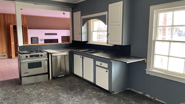 kitchen with plenty of natural light, stainless steel gas range oven, dark countertops, and white cabinetry