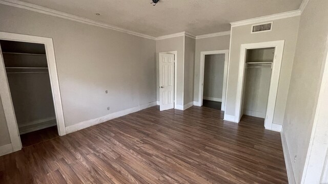 unfurnished bedroom with baseboards, crown molding, visible vents, and dark wood-type flooring