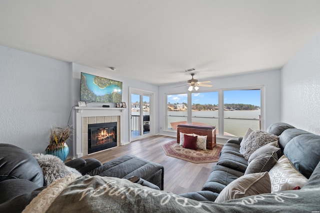 living area featuring a textured wall, a tile fireplace, a water view, wood finished floors, and visible vents