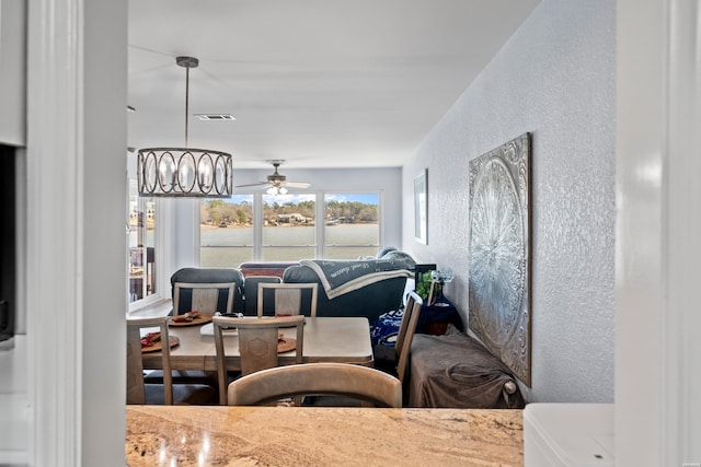 interior space featuring ceiling fan with notable chandelier, visible vents, and a textured wall