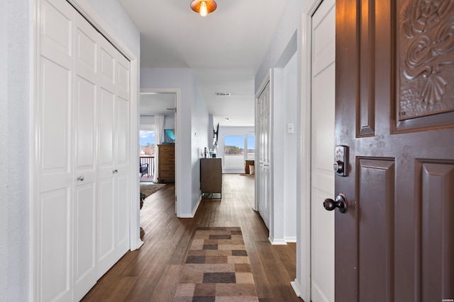 hall with dark wood-style flooring, visible vents, and baseboards