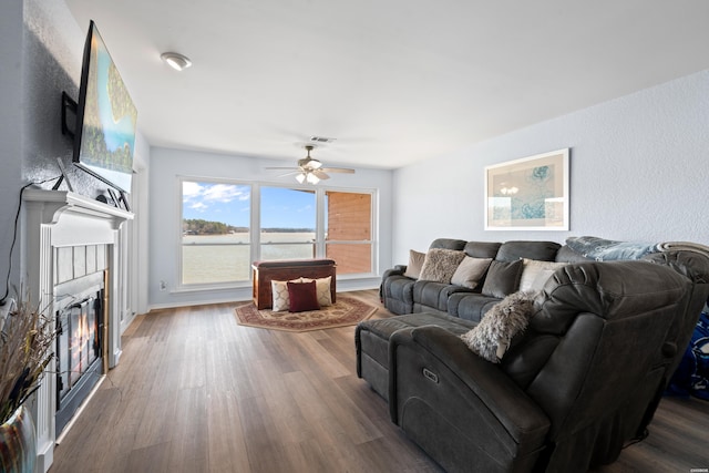 living area with visible vents, a tiled fireplace, a ceiling fan, wood finished floors, and baseboards