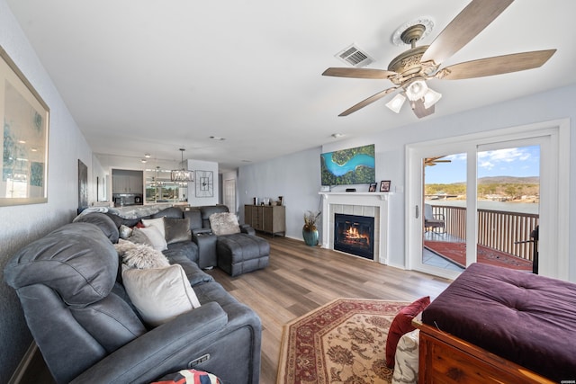 living room with light wood-style floors, visible vents, a tiled fireplace, and a ceiling fan