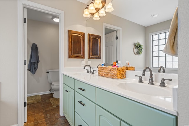 bathroom featuring double vanity, toilet, baseboards, and a sink
