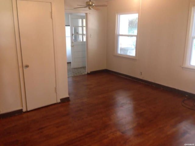 empty room featuring baseboards, dark wood finished floors, and a ceiling fan