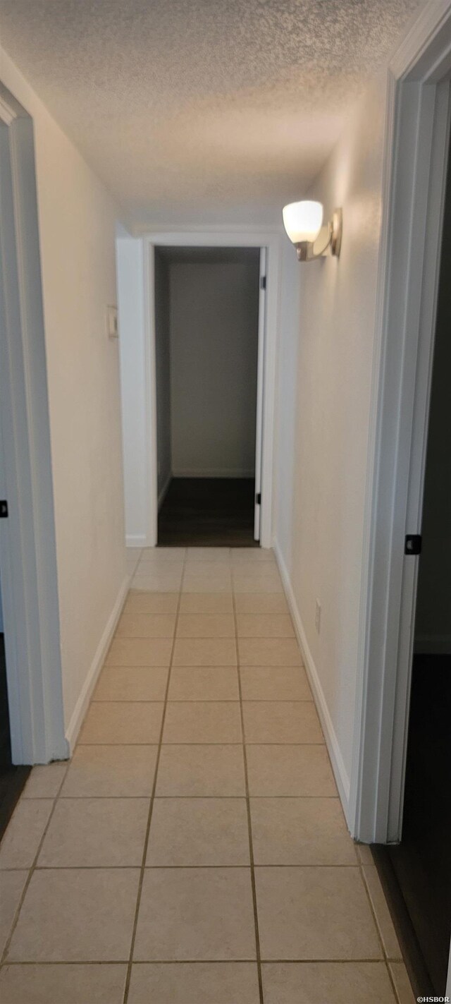 corridor featuring a textured ceiling, light tile patterned flooring, and baseboards