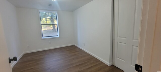 empty room featuring visible vents, baseboards, and dark wood finished floors