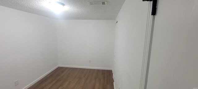 spare room with a textured ceiling, dark wood-type flooring, visible vents, and baseboards