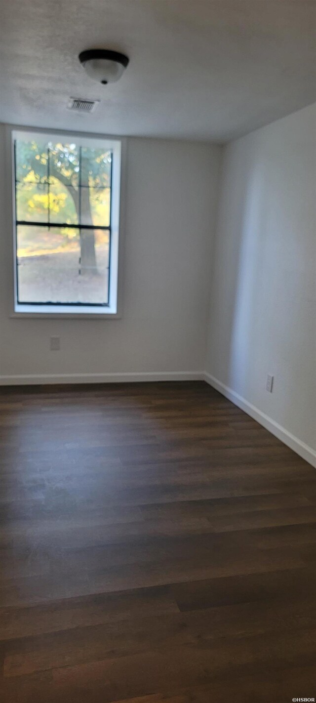 spare room featuring dark wood finished floors, visible vents, and baseboards