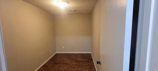 interior space featuring a textured ceiling, dark wood-style flooring, visible vents, and baseboards