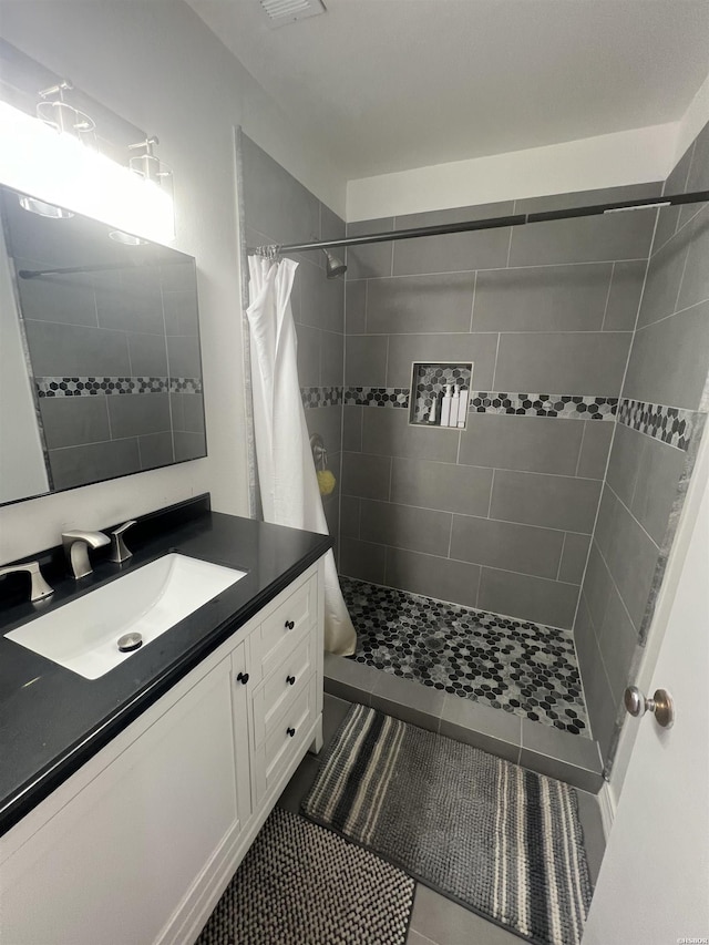 bathroom with tiled shower, vanity, and tile patterned floors