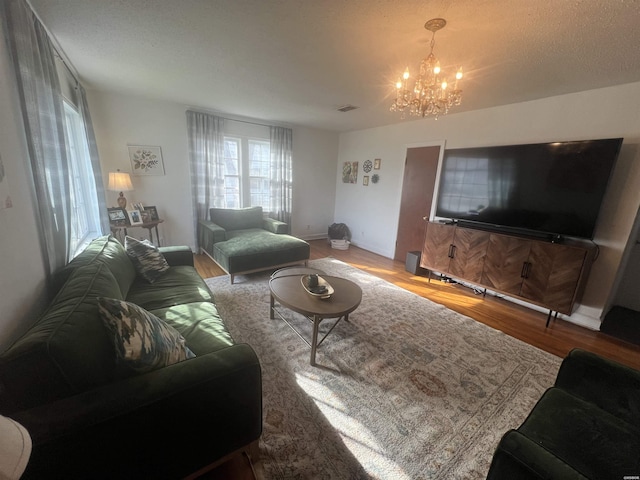 living room featuring baseboards, a notable chandelier, visible vents, and wood finished floors