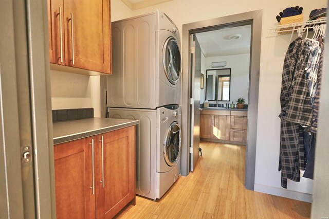 laundry area featuring light wood-type flooring, cabinet space, and stacked washer and clothes dryer