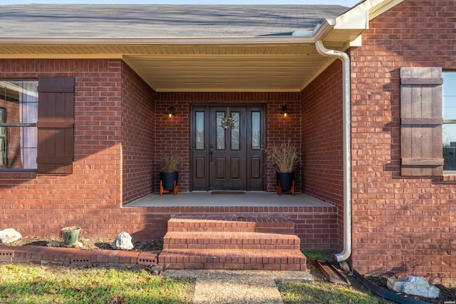 property entrance with roof with shingles, a porch, and brick siding