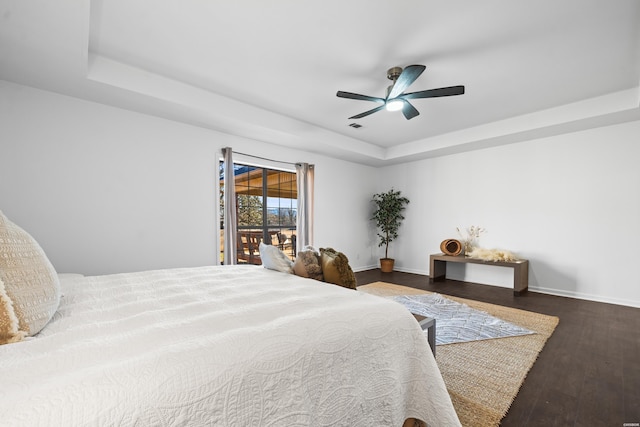 bedroom with a tray ceiling, visible vents, ceiling fan, wood finished floors, and baseboards