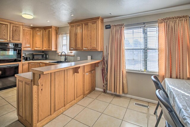 kitchen with visible vents, a peninsula, light countertops, black appliances, and a sink