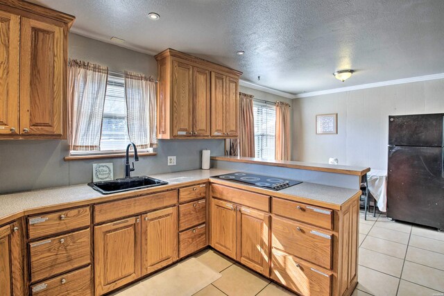 kitchen featuring brown cabinetry, a peninsula, light countertops, black appliances, and a sink