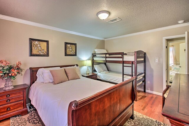 bedroom featuring light wood finished floors, baseboards, visible vents, ornamental molding, and a textured ceiling