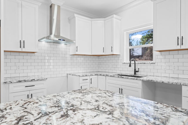 kitchen featuring decorative backsplash, ornamental molding, white cabinets, a sink, and wall chimney exhaust hood