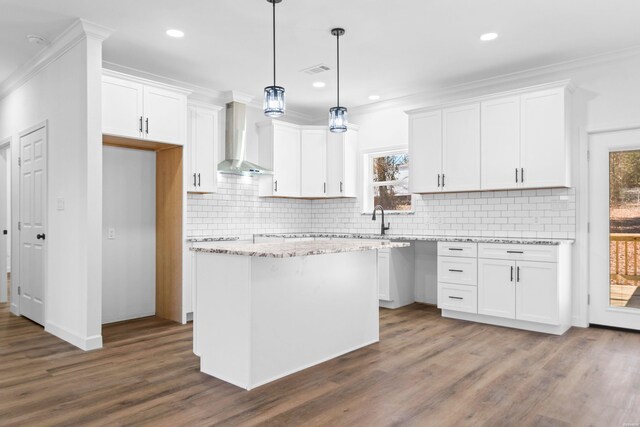 kitchen with pendant lighting, wall chimney exhaust hood, white cabinetry, and a center island