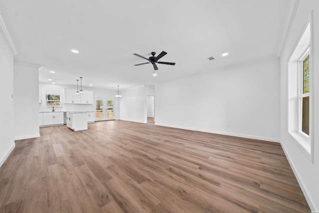 unfurnished living room featuring baseboards, light wood finished floors, visible vents, and crown molding