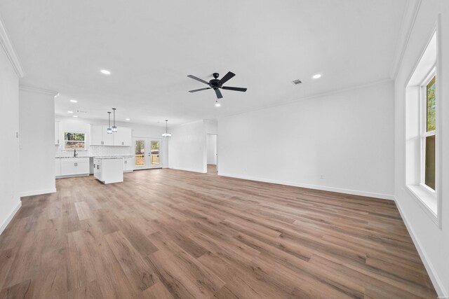 unfurnished living room featuring baseboards, light wood finished floors, visible vents, and crown molding