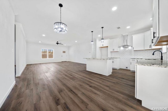 kitchen featuring wall chimney exhaust hood, open floor plan, a center island, white cabinetry, and a sink